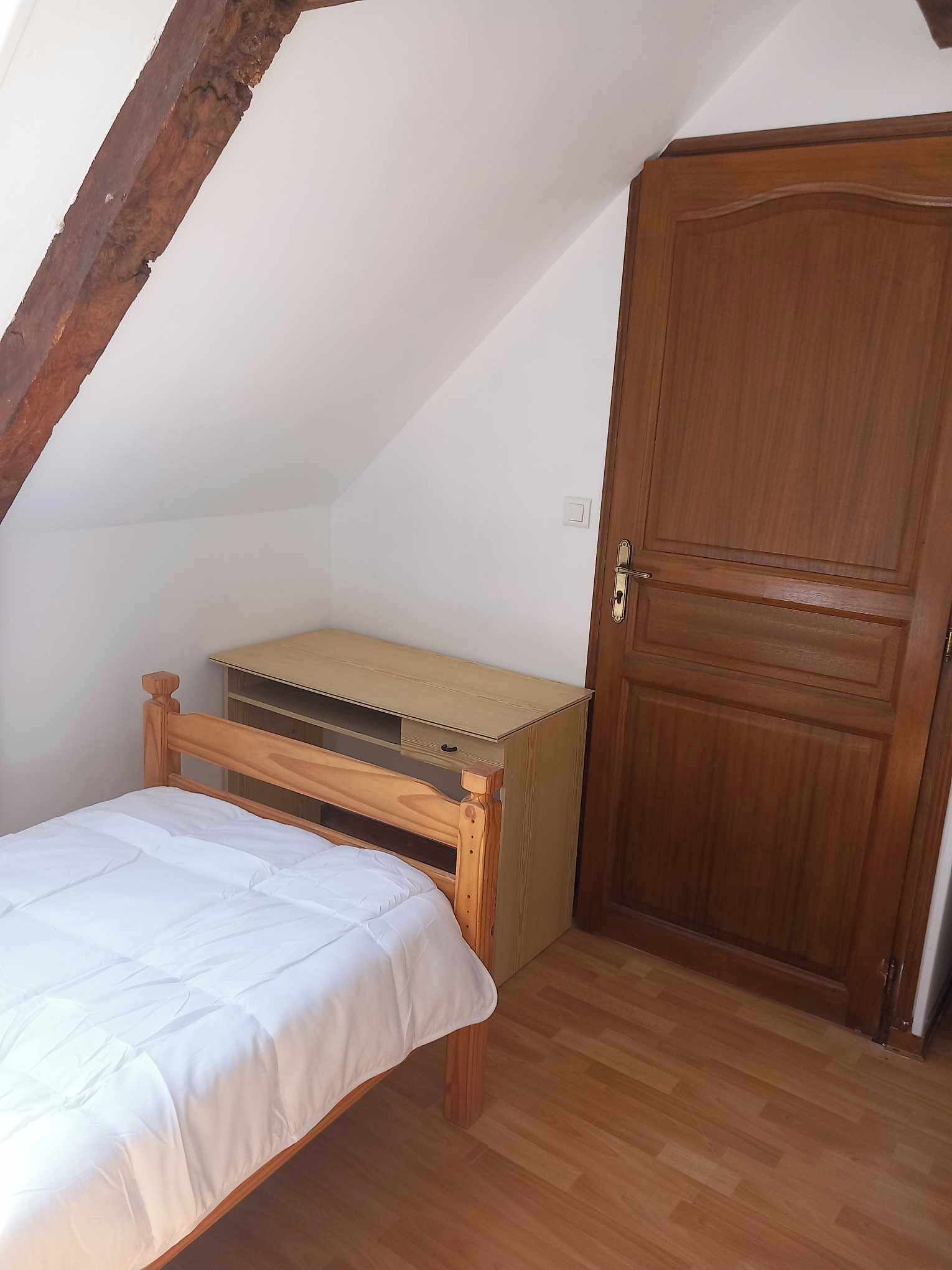 A small, single-bed room with a wooden headboard and a wooden bench.