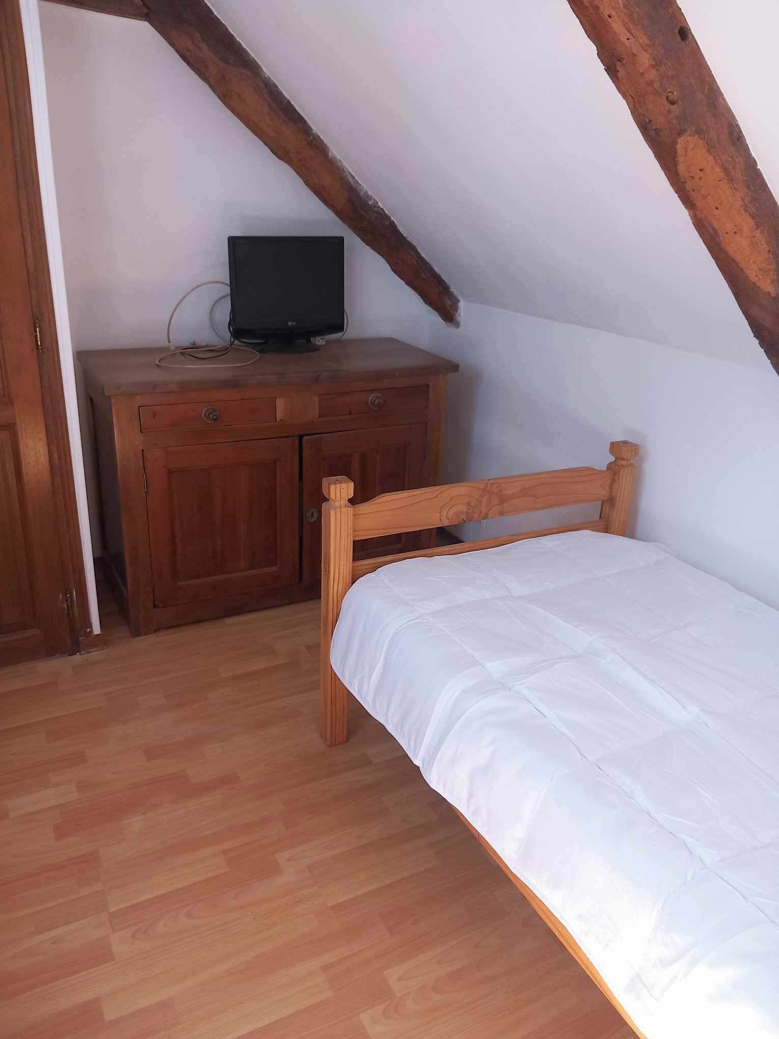 A small, single-bed room with a wooden bed and a wooden desk with a television.