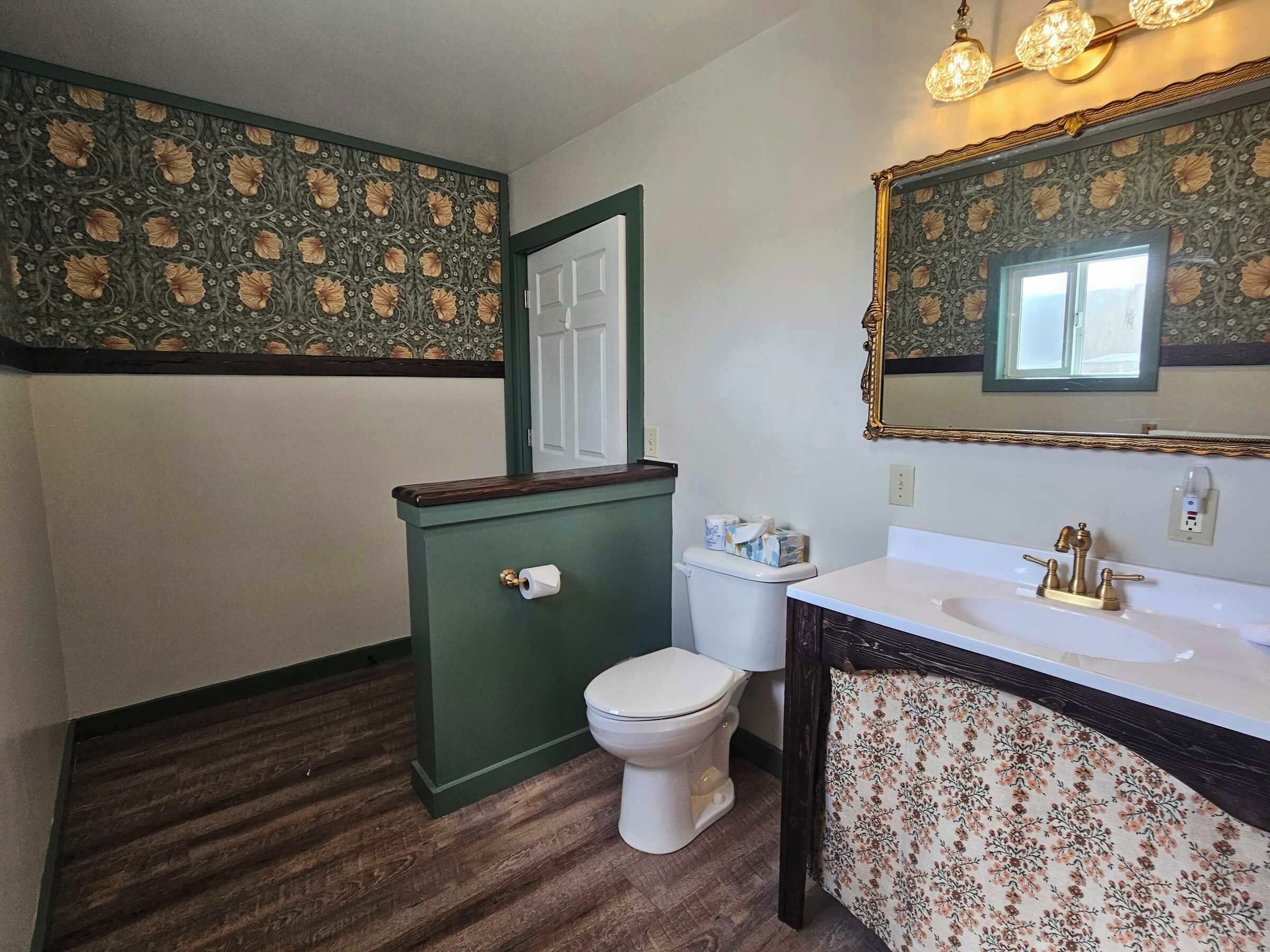 Un baño con tocador verde, inodoro blanco y espejo con marco decorativo.