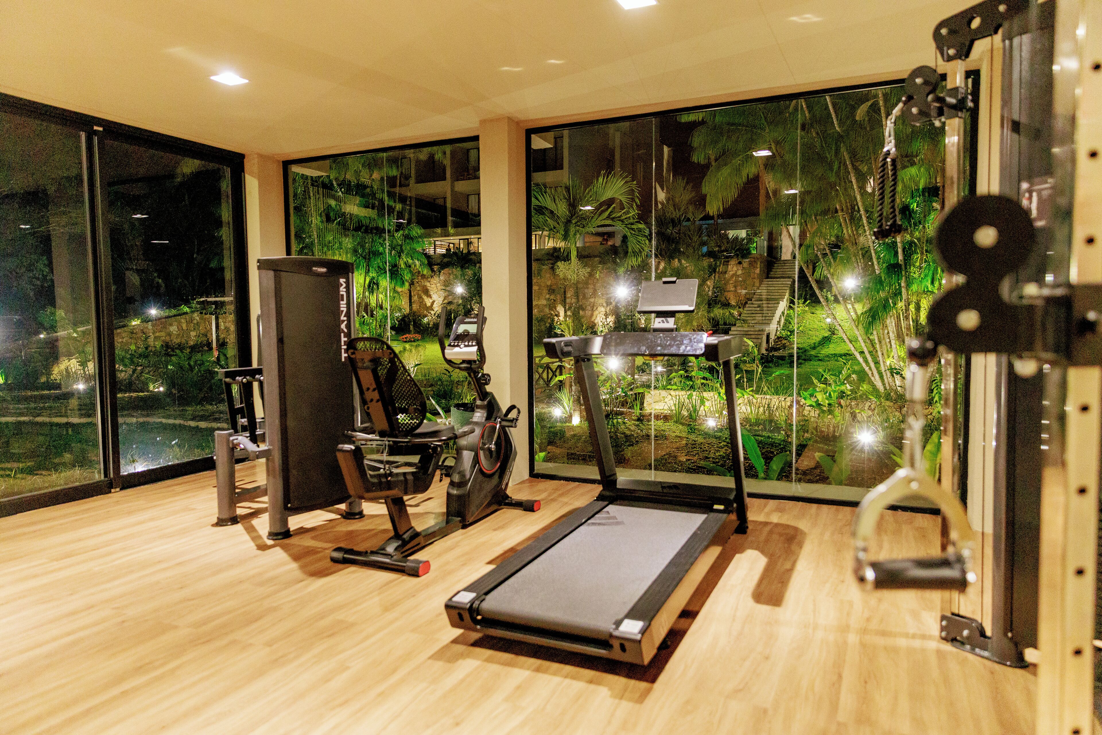 Une salle de sport équipée de matériel d’exercice, dotée de grandes fenêtres et offrant une vue sur la verdure.