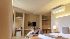Una habitación de hotel moderna con una cama, un rincón de lectura con un sofá, un televisor y una kitchenette pequeña.