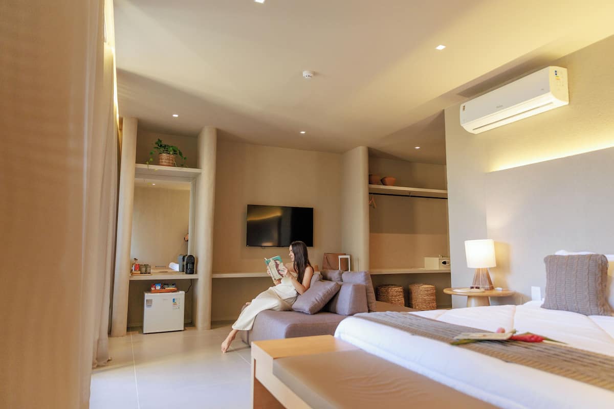 Ein modernes Hotelzimmer mit einem Bett, einer Leseecke mit Sofa, einem Fernseher und einer kleinen Küchenzeile.
