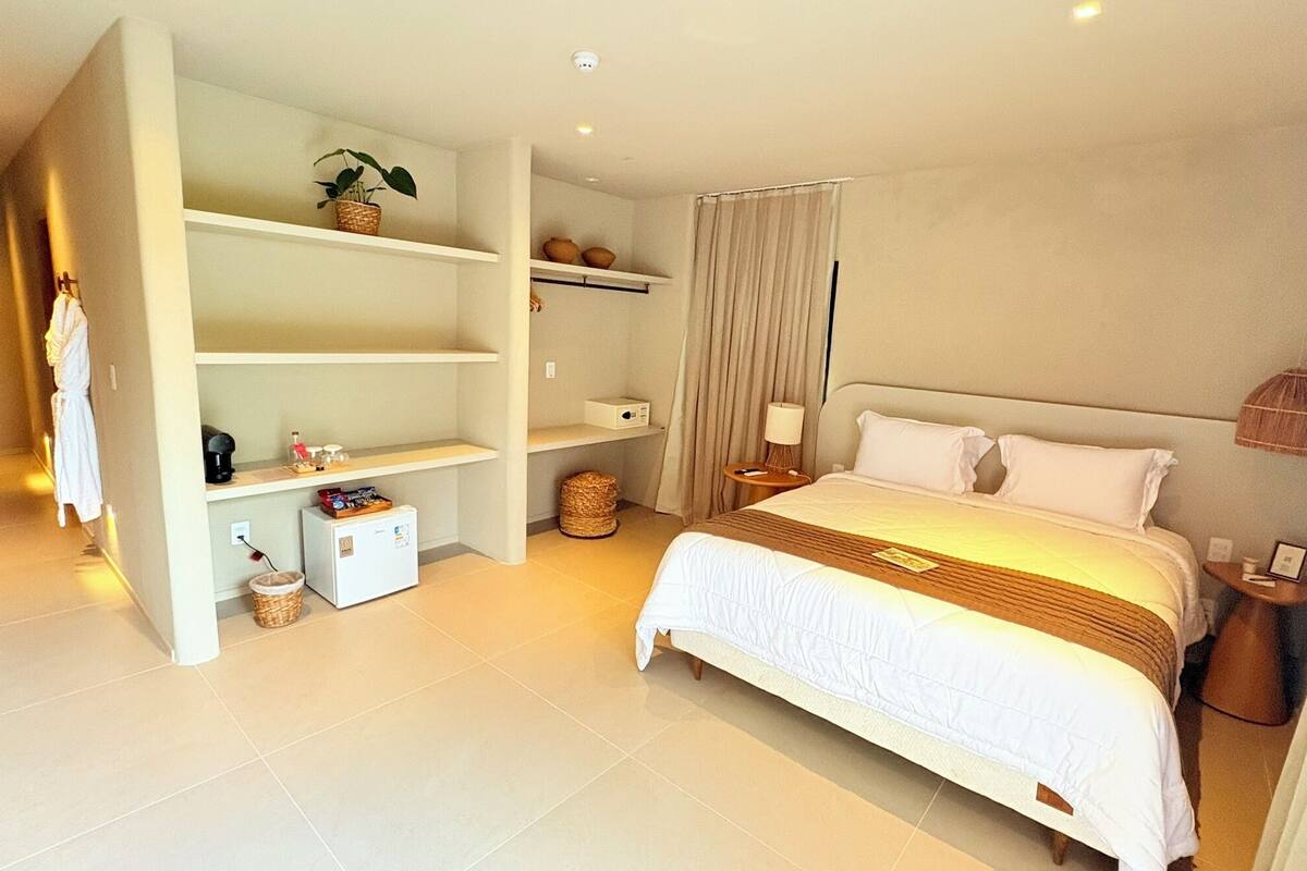 Ein Hotelzimmer mit einem großen Bett, einem Schrank, einem kleinen Kühlschrank, einem Nachttisch mit Lampe und einem Vorhang.