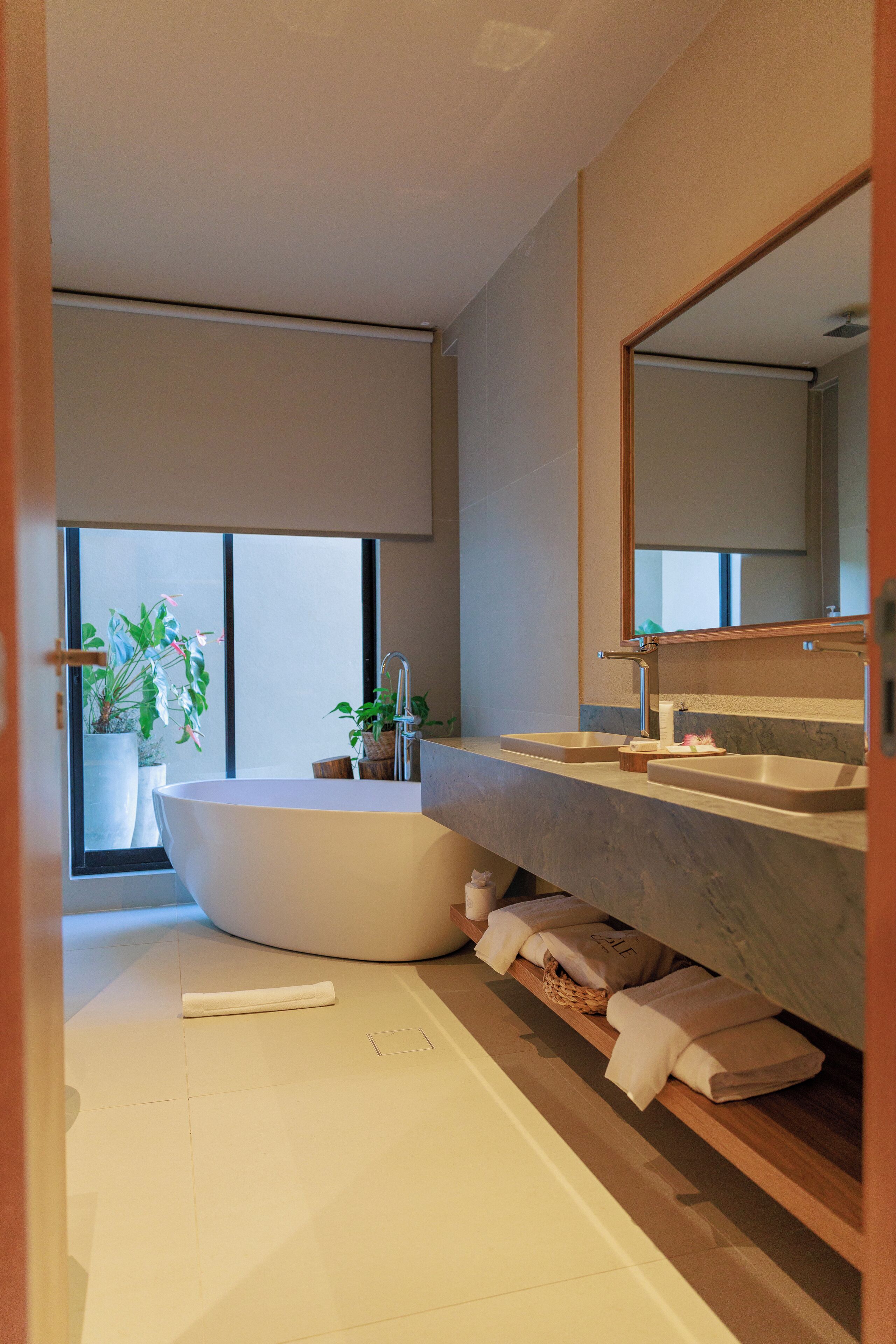 Ein modernes Badezimmer mit einer freistehenden Badewanne, einem großen Spiegel und einem Fenster für natürliches Licht.