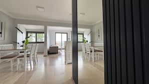 Una habitación amplia con un ventanal grande, un comedor con mobiliario blanco y vistas al exterior.