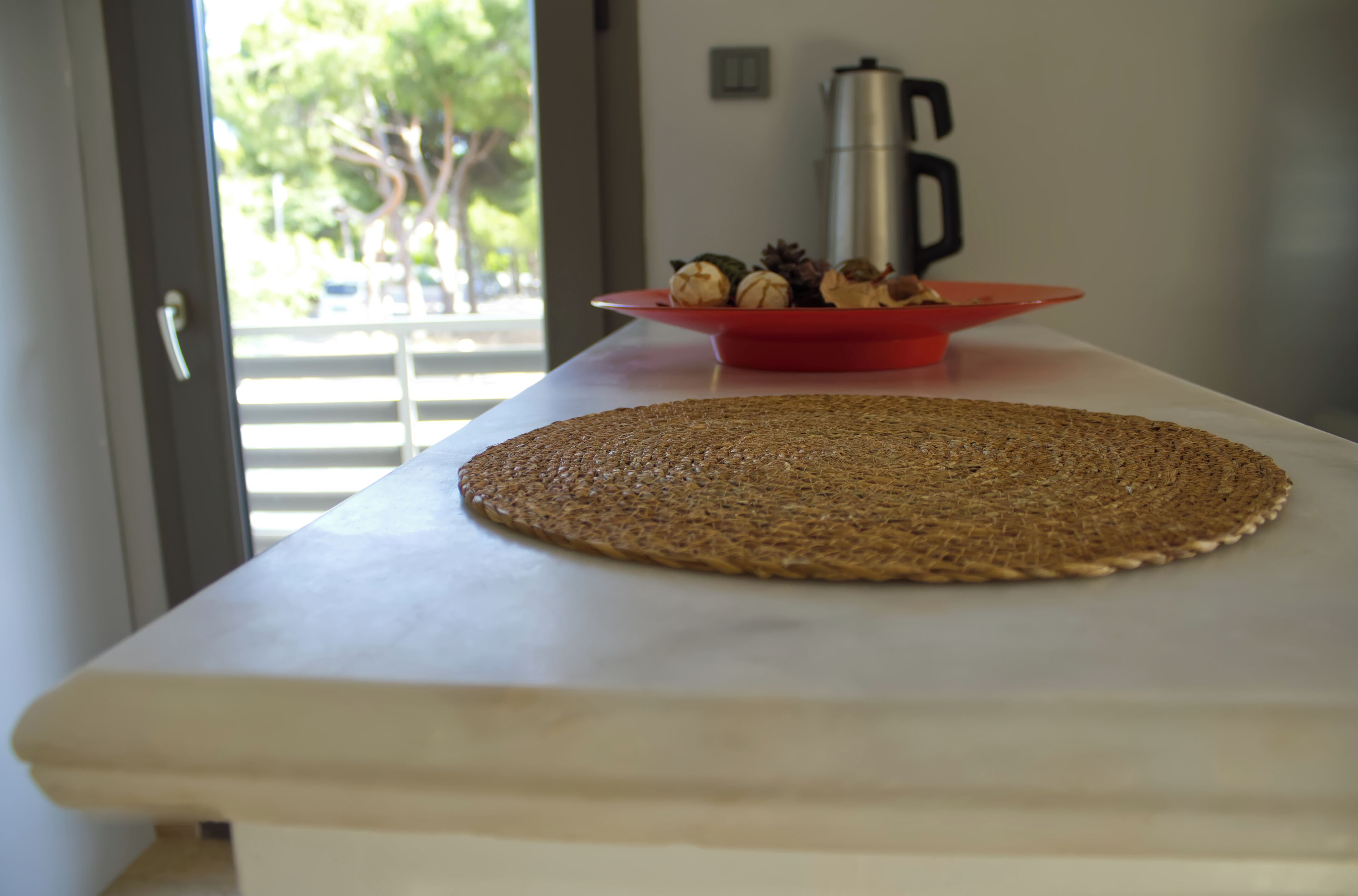 A kitchen counter with a woven placemat, a red plate with food items, and a coffee maker.