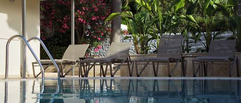 Piscina com espreguiçadeiras e um muro de pedra com flores cor-de-rosa.