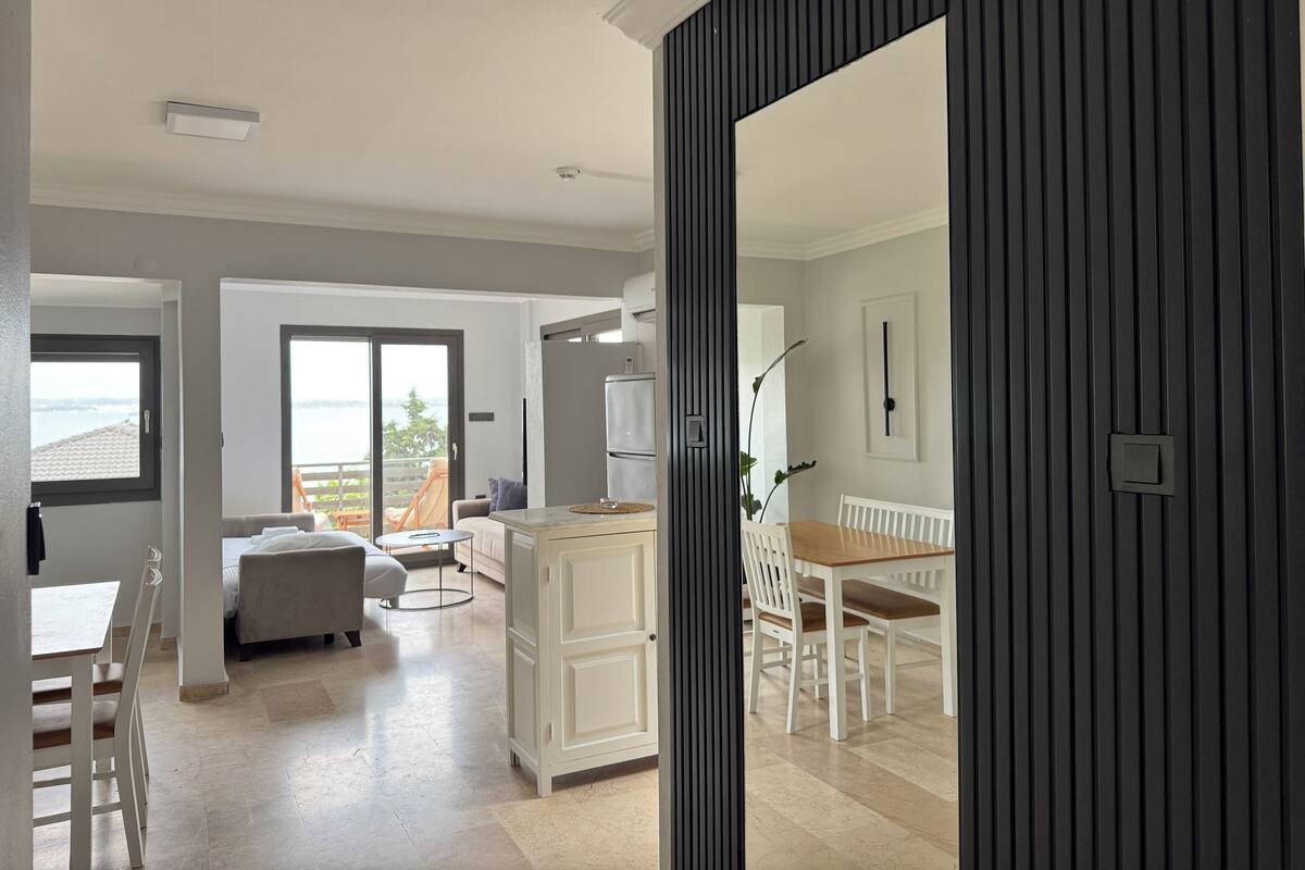 A modern living room with a dining area, a kitchen, and a balcony with a view.