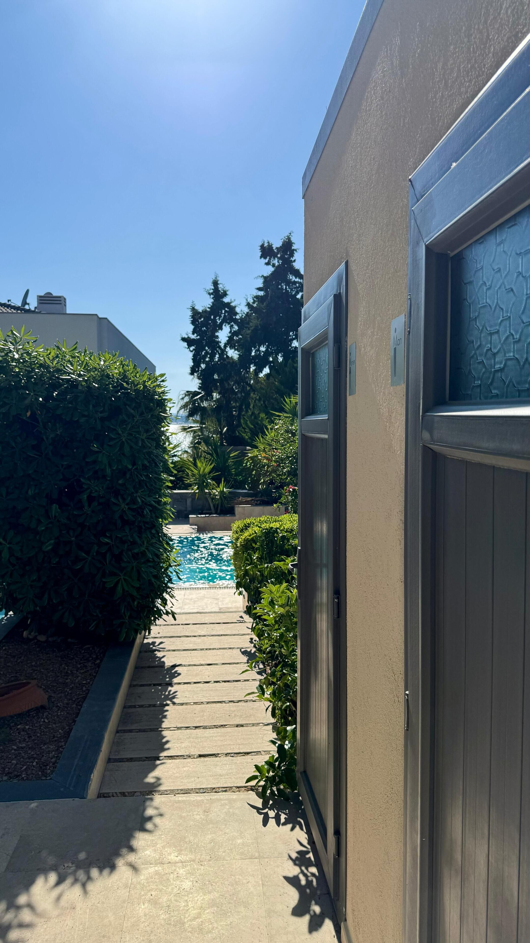 A pathway leading to a swimming pool with a view of trees and a building in the background.