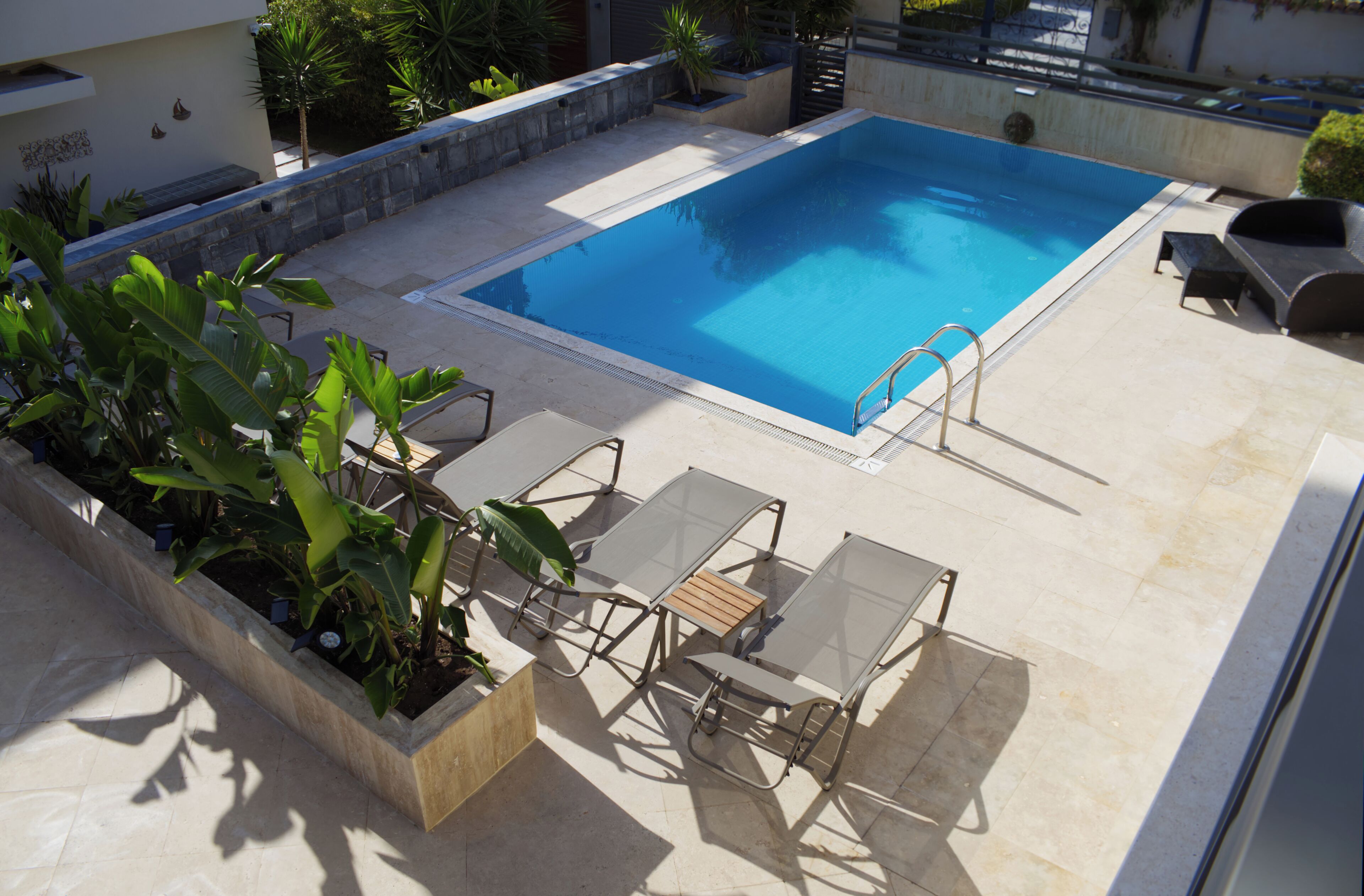 Piscina en la azotea con superficie de agua azul cristalina, rodeada de sillas de descanso y un jardín con plantas tropicales.