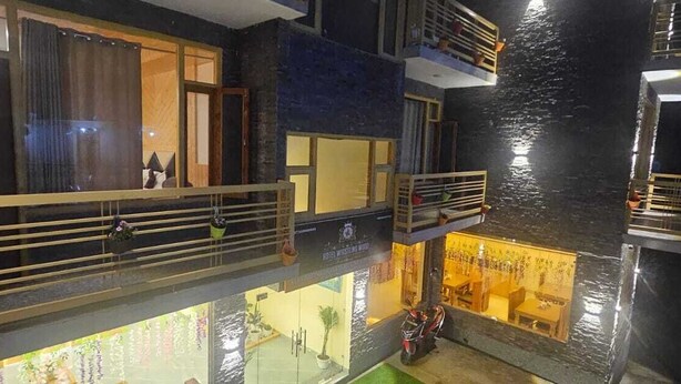 A multi-level hotel with balconies, a restaurant, and a view of the water. - Whistling Wood by Jai Maa Jwala Groups (Manali)