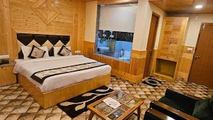 A wooden-paneled room with a bed, a small table, and a view of a bathroom through a window. - Whistling Wood by Jai Maa Jwala Groups (Manali)