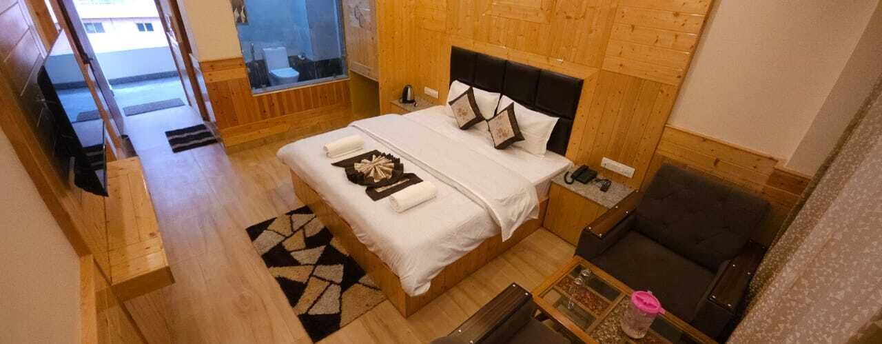 A hotel room with a wooden floor, a bed with white linens, a nightstand, a chair, and a small table with a pink object.