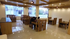 A spacious dining area with wooden furniture and large windows. - Whistling Wood by Jai Maa Jwala Groups (Manali)