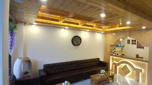 A reception area with a wooden ceiling, a reception desk, a sofa, and a wall clock. - Whistling Wood by Jai Maa Jwala Groups (Manali)