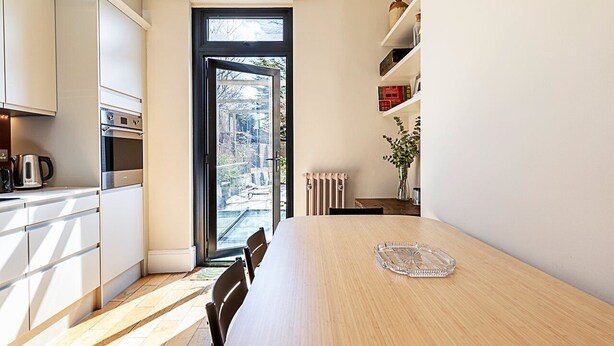 A modern kitchen with white cabinets, a large dining table, and a view through a glass door to the outside.