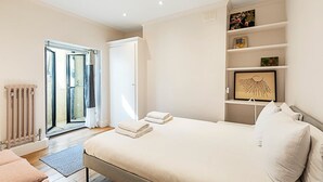 A bedroom with a bed, a radiator, a door to a balcony, and a shelf with framed pictures.