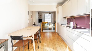 A modern kitchen with white cabinets, a wooden dining table, and a glass partition.