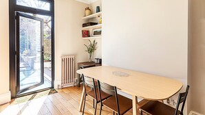 A dining area with a table and chairs, a radiator, a shelf with decorative items, and a door leading to an outdoor area.