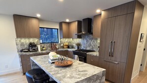 A modern kitchen with a marble island, wooden cabinets, and a large refrigerator.