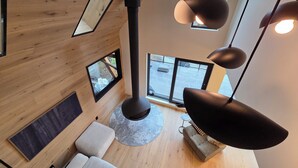 A modern interior with a high ceiling, wooden panel walls, a central black column, and multiple hanging pendant lights.