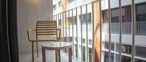 Un balcon avec une chaise en bois et une petite table, un sol carrelé de carreaux blancs et une vue sur un immeuble doté de balcons.