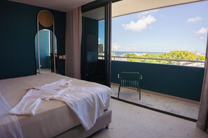 Une chambre d’hôtel avec un lit, une chaise, un grand miroir et un balcon donnant sur la mer.