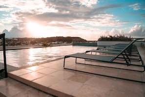 A rooftop pool area with lounge chairs and a view of a cityscape.