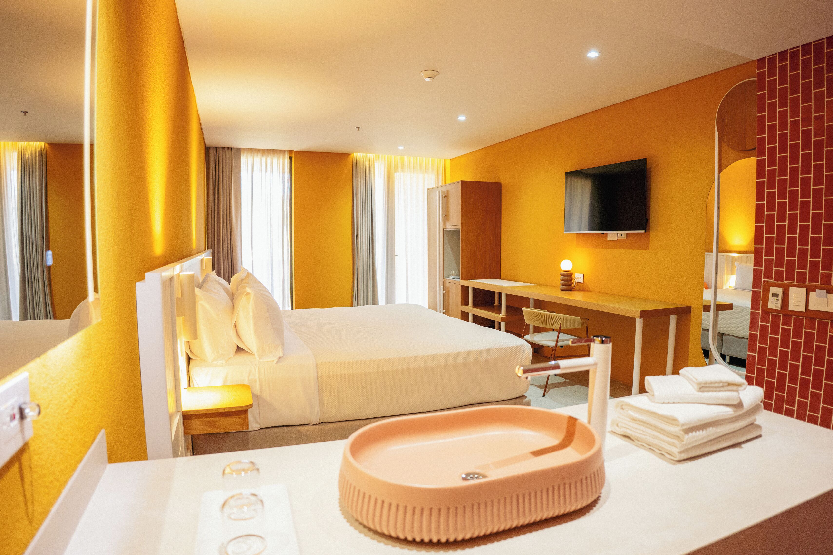 Habitación de hotel con cama, escritorio, espejo y lavabo con espejo redondo.