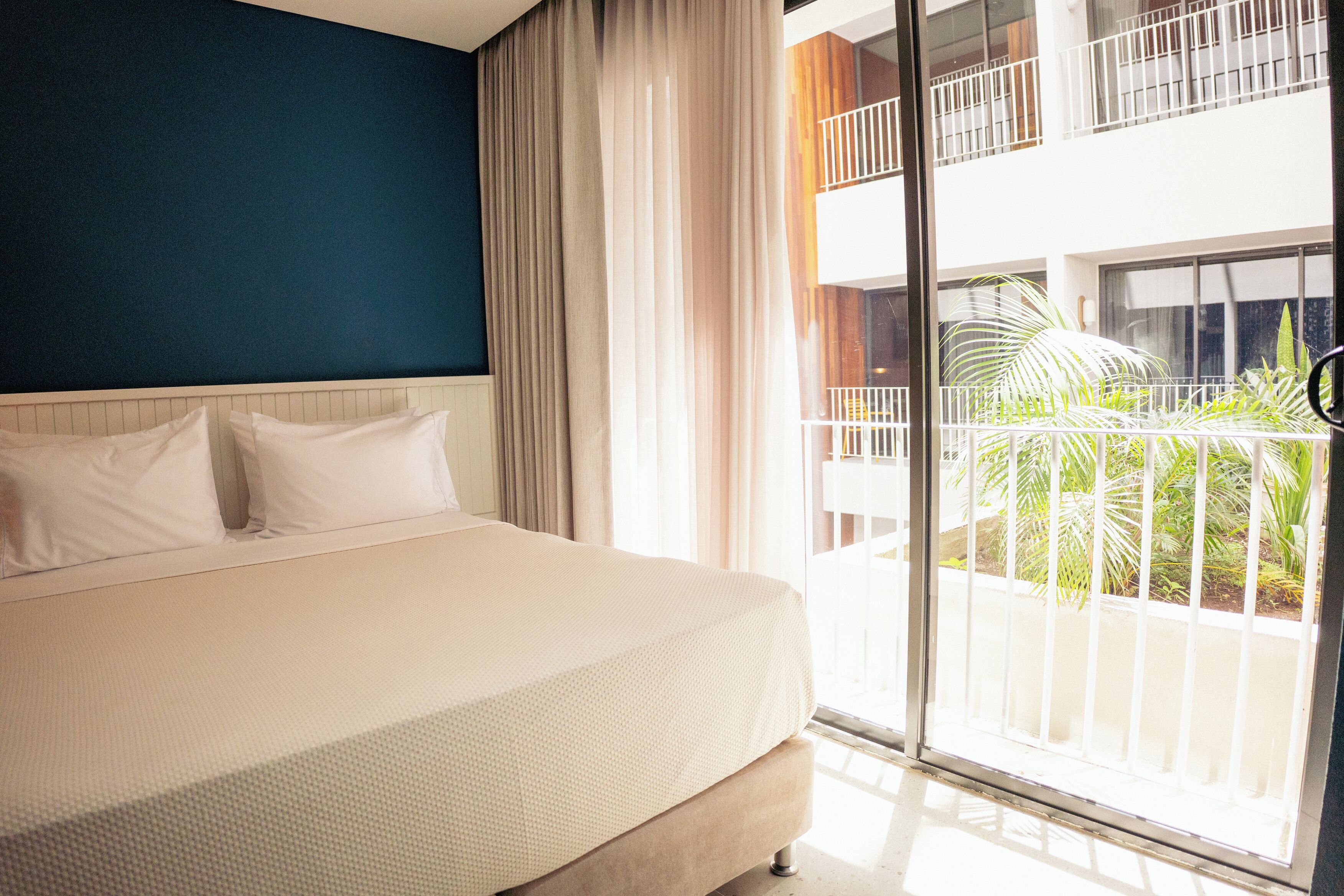 A hotel room with a bed, a large window, and a view of the outside balcony.