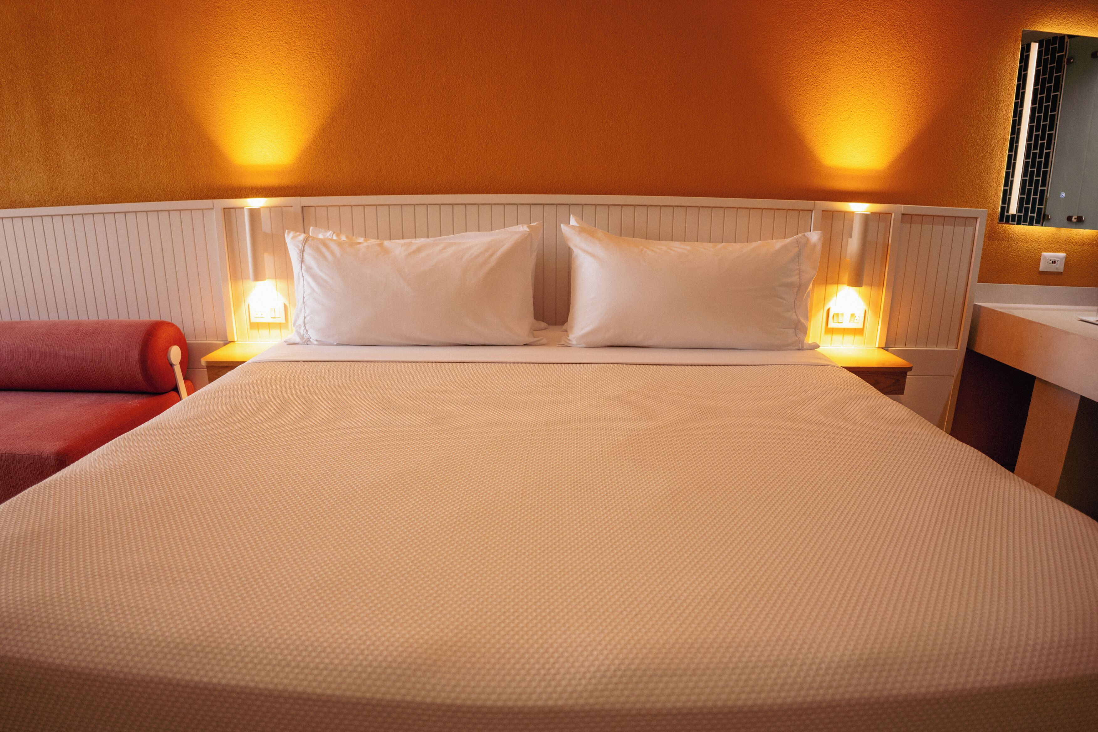 A hotel room with a large bed, two bedside lamps, a red chair, and a wooden nightstand.