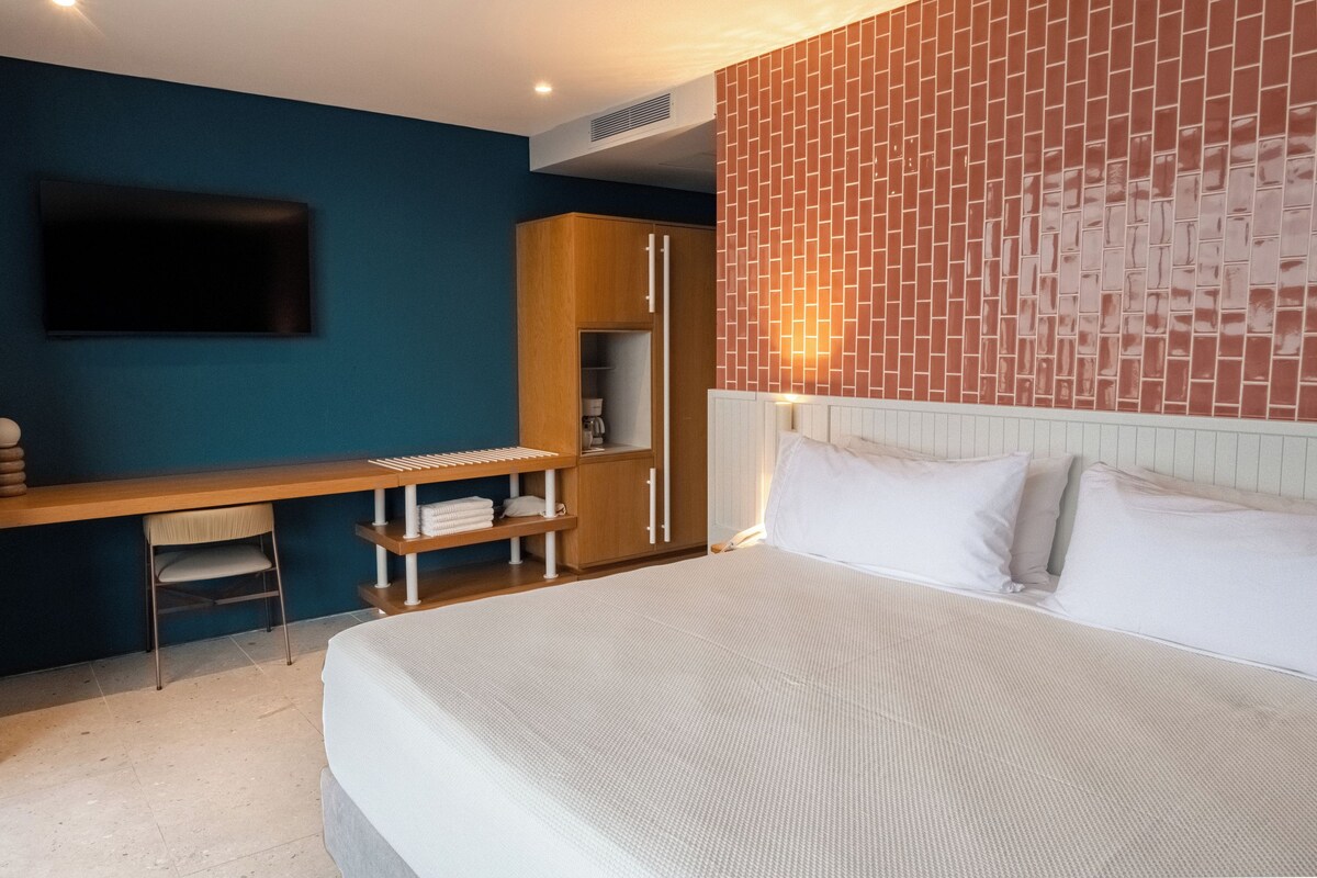 A hotel room with a bed, a desk, a chair, a wardrobe, and a TV mounted on the wall.