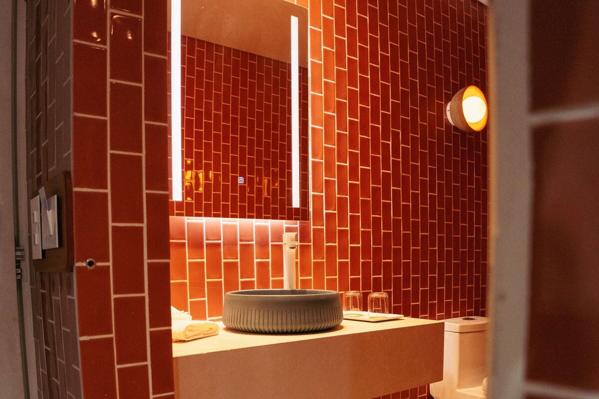 A bathroom with red-tiled walls, a white sink, and a mirror.