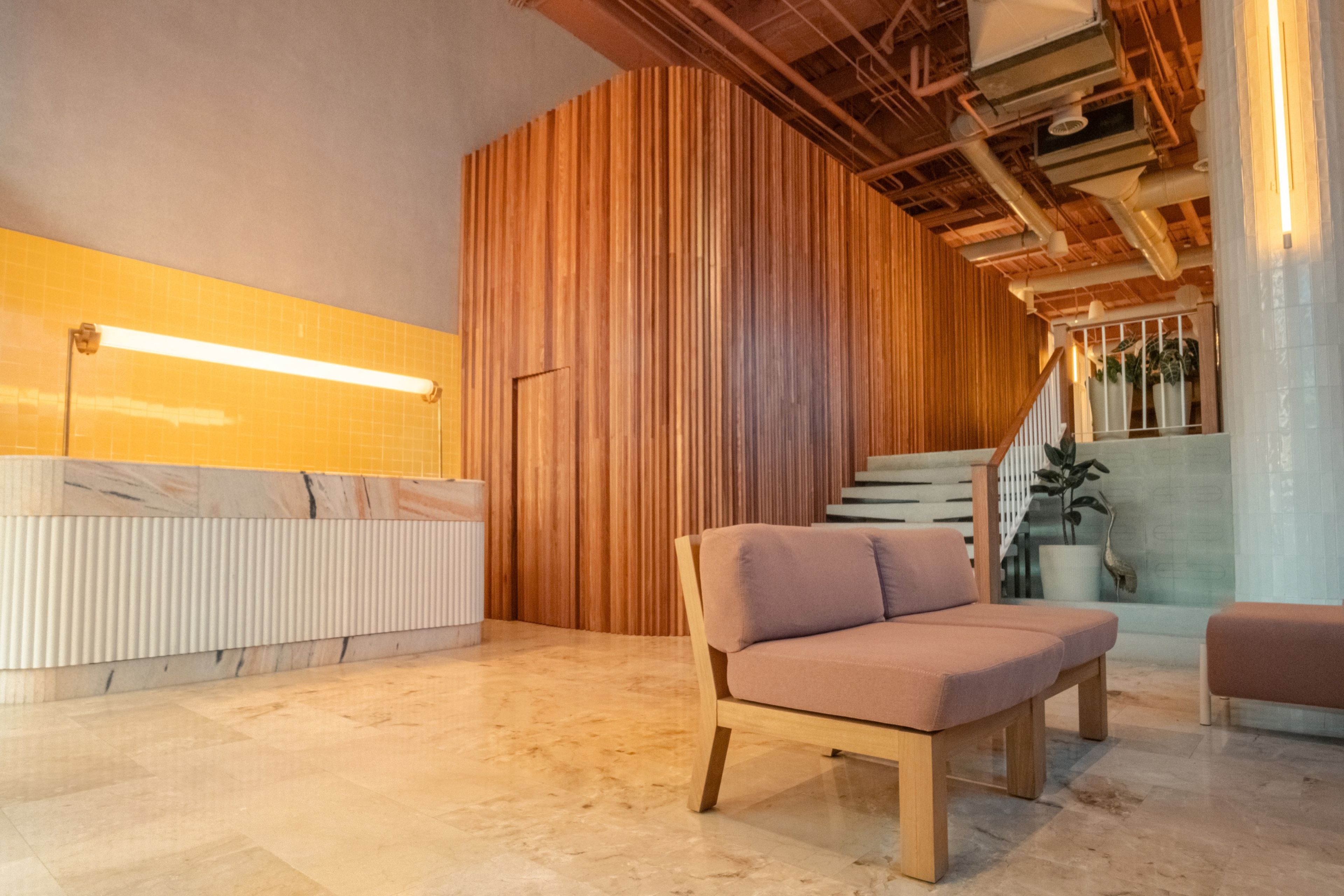 Een modern interieur met een houten accentmuur, een receptiebalie, een comfortabele zithoek en een trap naar een hoger gelegen verdieping.