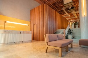 Egy modern belső tér, melynek része egy fa borítású hangsúlyfal, egy recepciós pult, kényelmes ülősarok és egy lépcső, amely a felső szintre vezet.