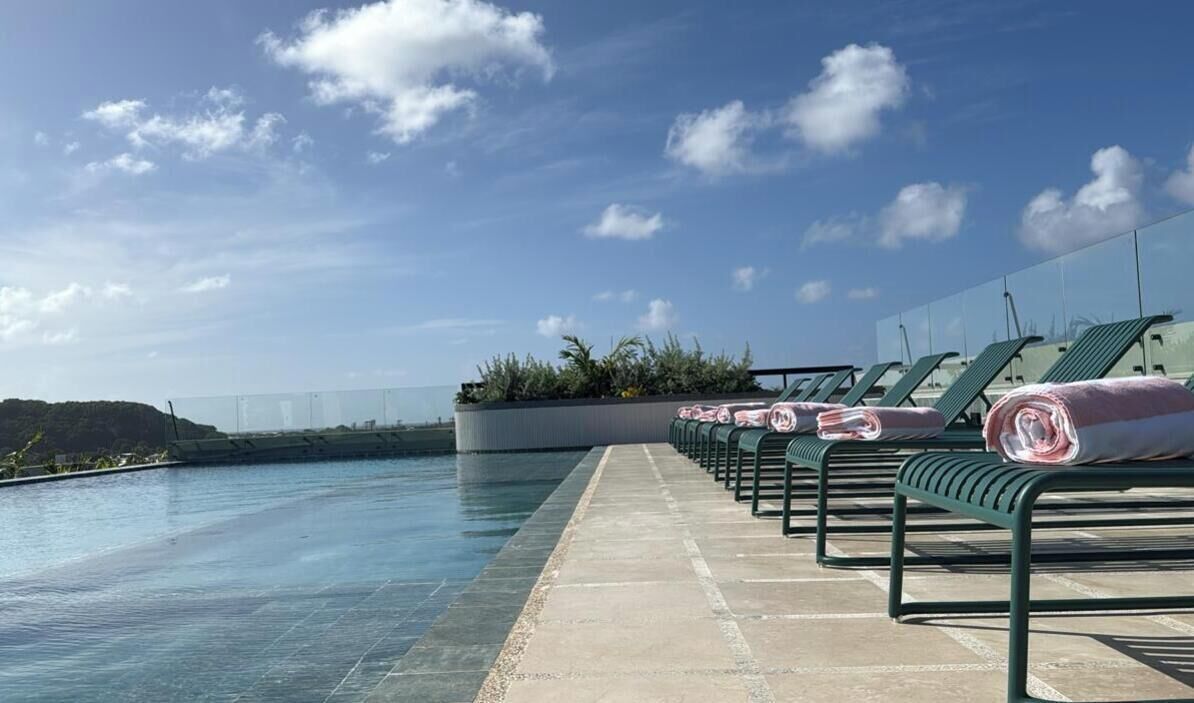 Área de piscina en la azotea con sillones de descanso y toallas, con vistas a una masa de agua y un paisaje lejano.