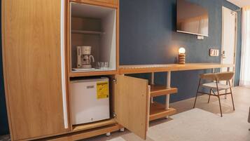 Una kitchenette compacta con cafetera, refrigerador pequeño y una silla.