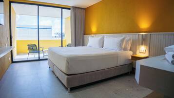 A hotel room with a large bed, a nightstand, a chair, and a view of the outside balcony.