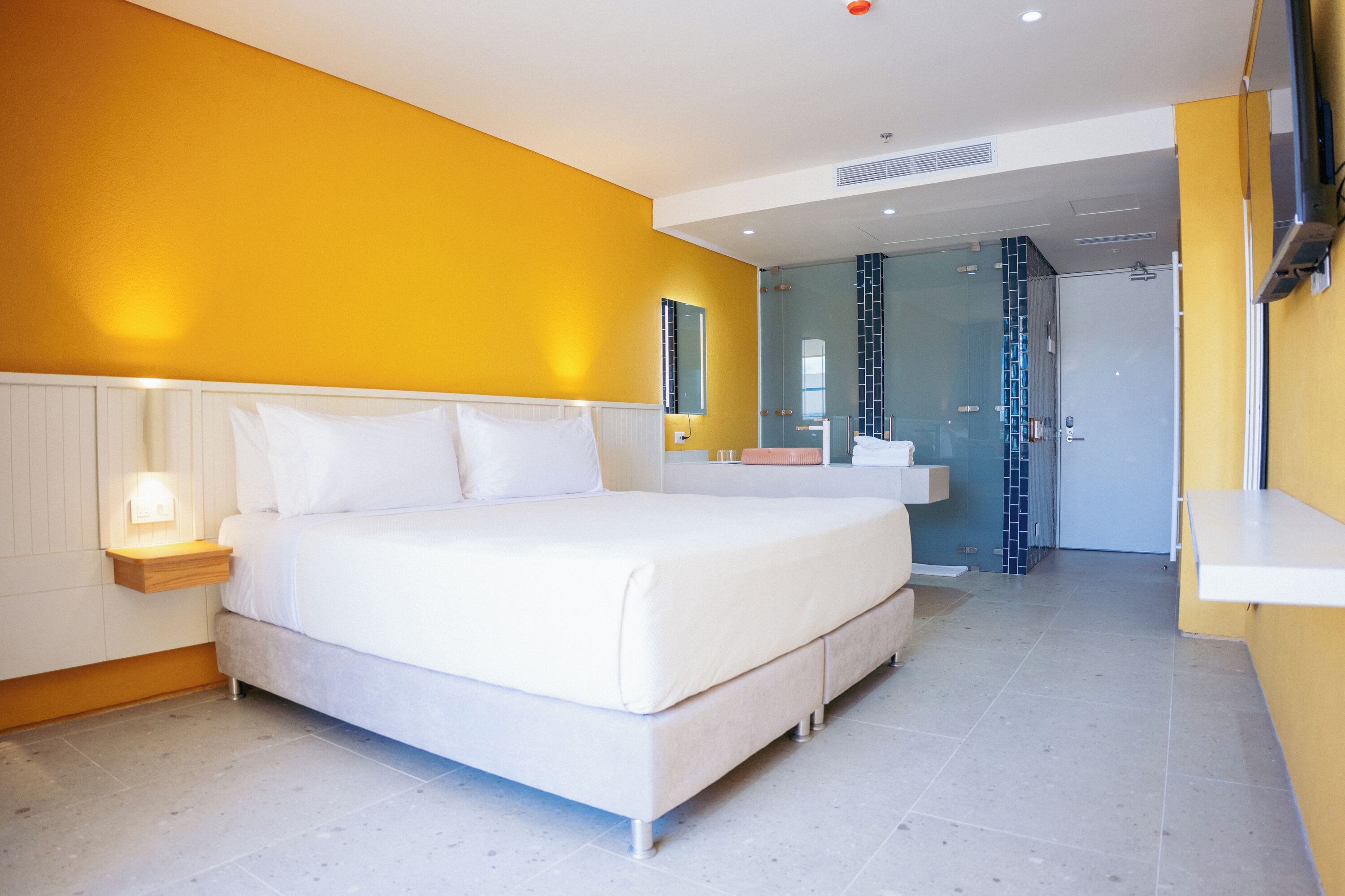 A modern bedroom with a large bed, bedside tables, and a bathroom visible through an open door.