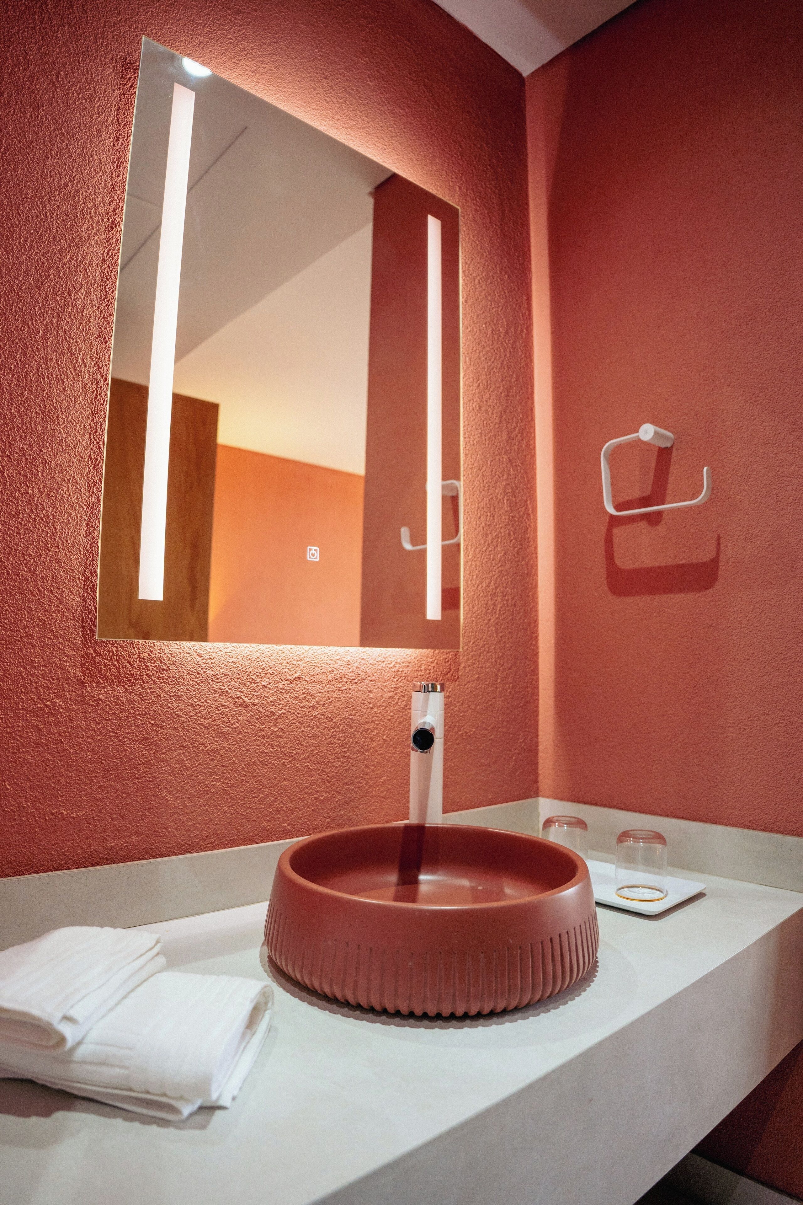 Un baño con un lavamanos redondo, un espejo y un perchero para toallas.