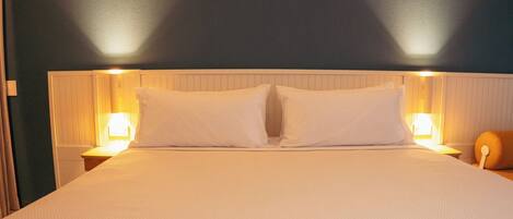 Una cama bien hecha con sábanas blancas y dos lámparas de noche a ambos lados.