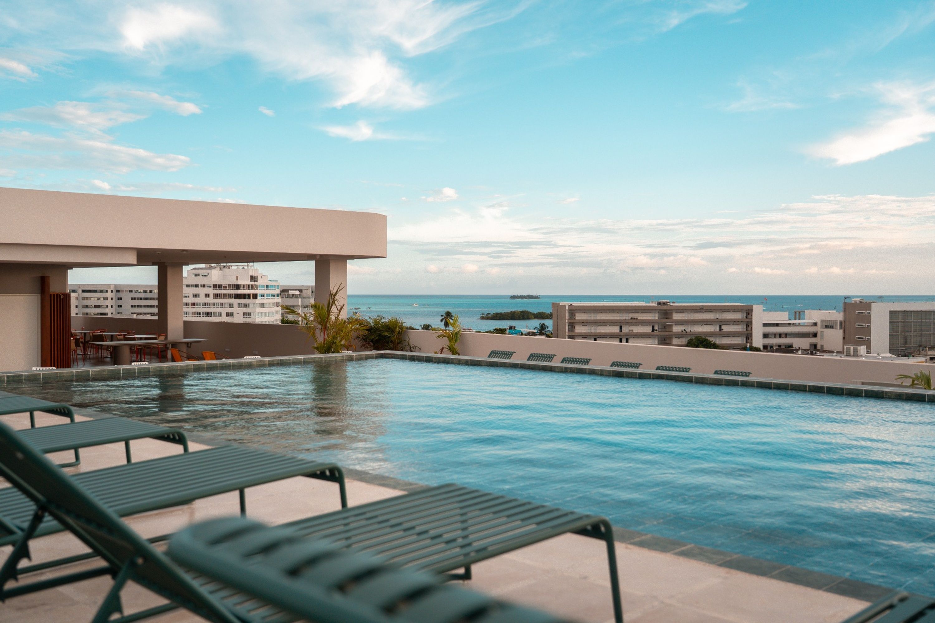 Una piscina a la terrassa amb gandules, vista a l'oceà i edificis al fons.