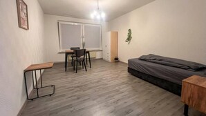 A small, sparsely furnished room with a bed, a desk, and a chair.