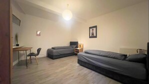 A small, well-lit room with two single beds, a desk with a chair, and a radiator.