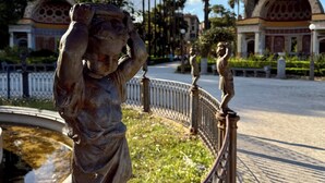 A statue of a figure with raised hands, a fountain, and a pathway with a fence and palm trees in the background. - Appartamenti Pellegrino (Palermo)