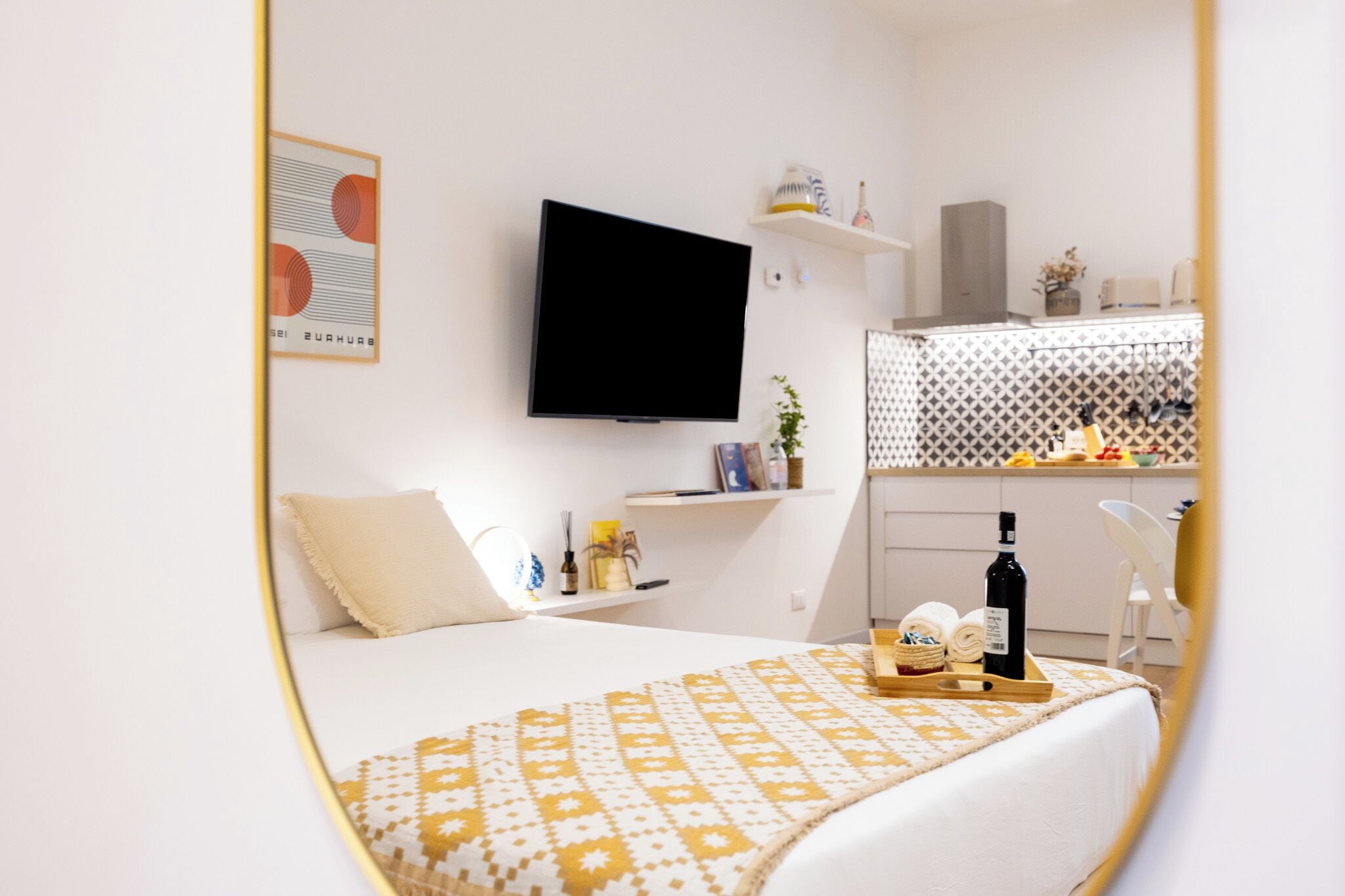 A modern hotel room with a bed, a flat-screen TV, a small kitchen area, and a dining table.