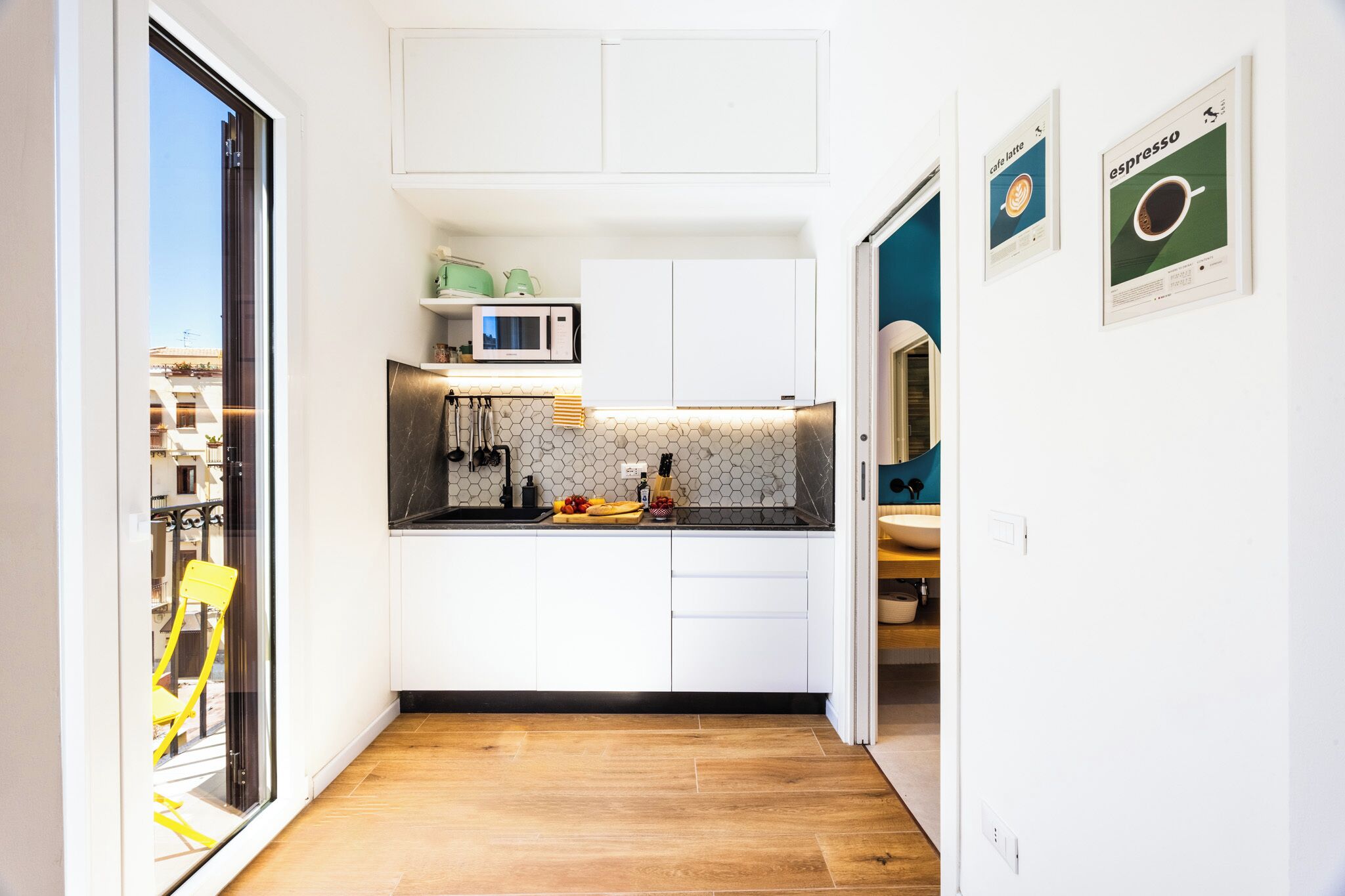 Una cocina compacta con armarios blancos, un microondas y un salpicadero hexagonal.