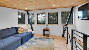 A modern living room with a blue sofa, a small wooden table, and a staircase with a black railing.