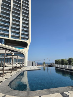Un hotel moderno con piscina infinita en la azotea, fachada de vidrio curvada y vistas al océano.