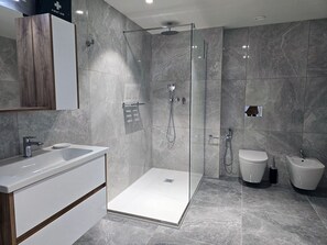 Un baño moderno con cabina de ducha de vidrio, un lavabo blanco y un inodoro.